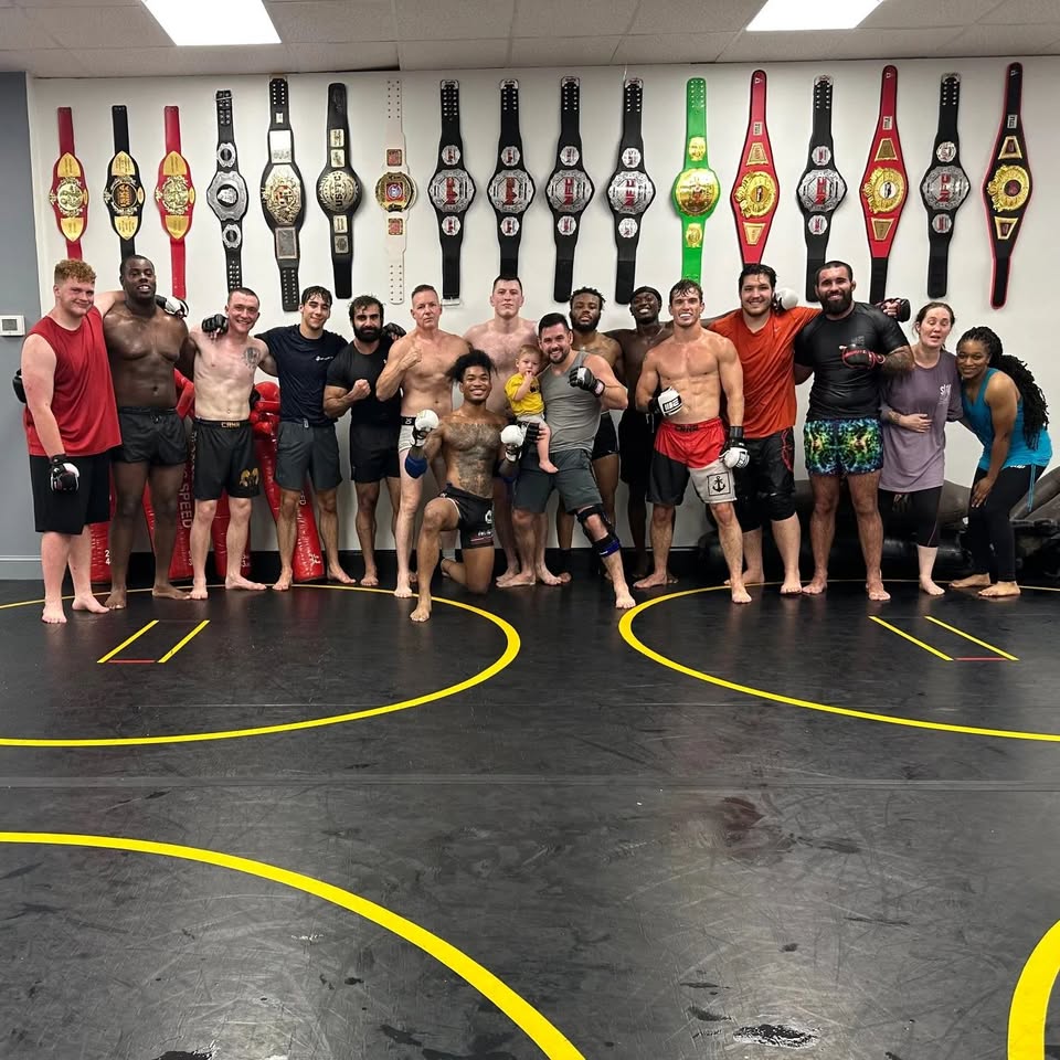 The Faglier's MMA team on the mat in front of a wall lined with championship belts